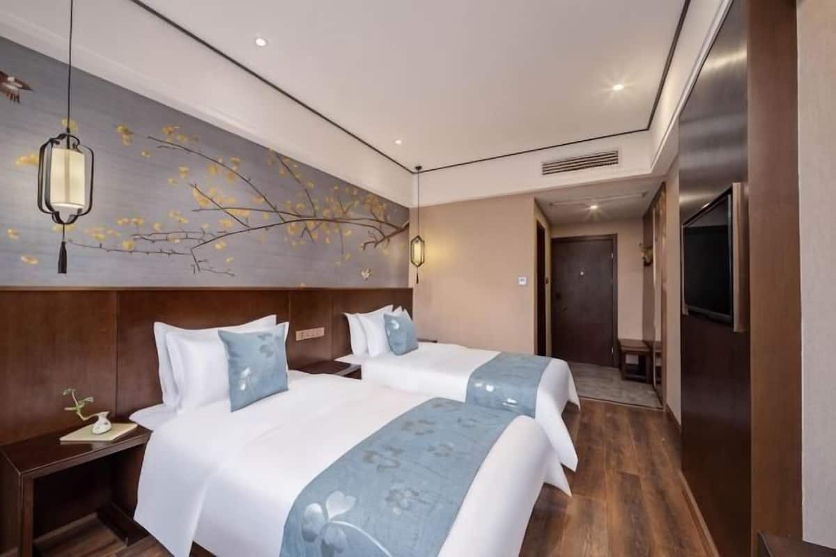 A hotel room with two beds, a wooden headboard, a wall-mounted TV, and a decorative branch artwork.