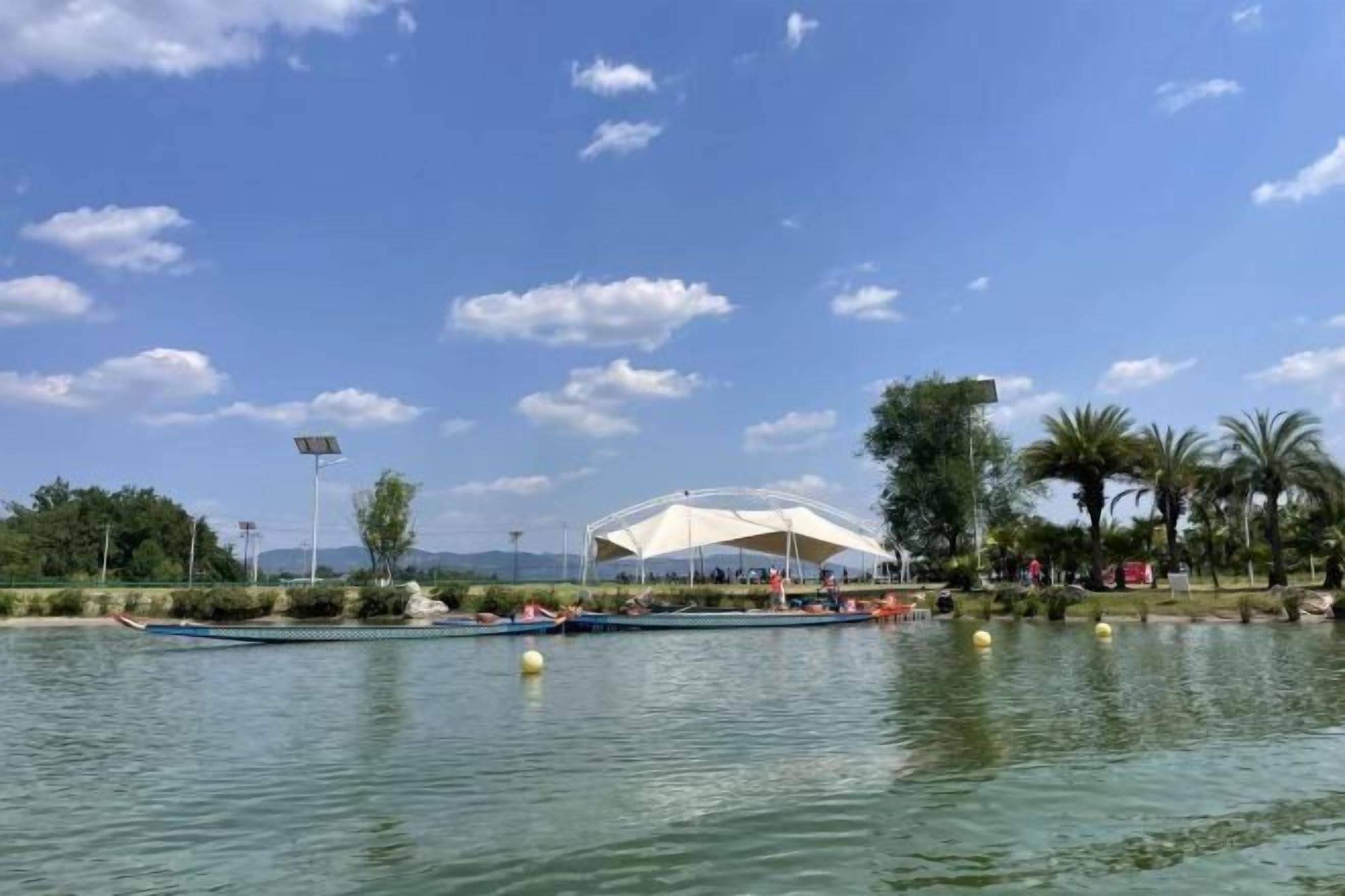A calm lake with boats, a covered pavilion, and palm trees.