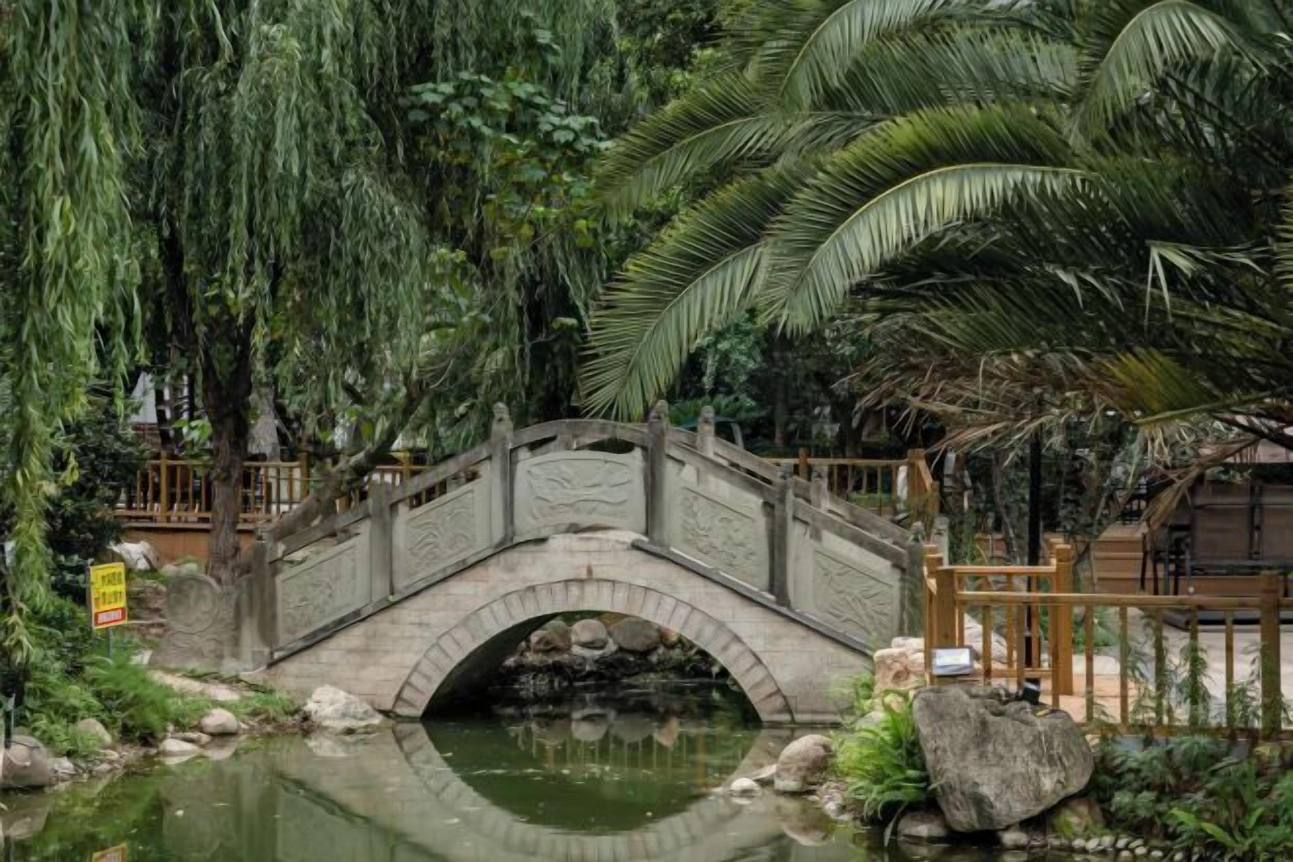 Un pont de pierre enjambant un étang, entouré de verdure et bordé d’une clôture en bois.