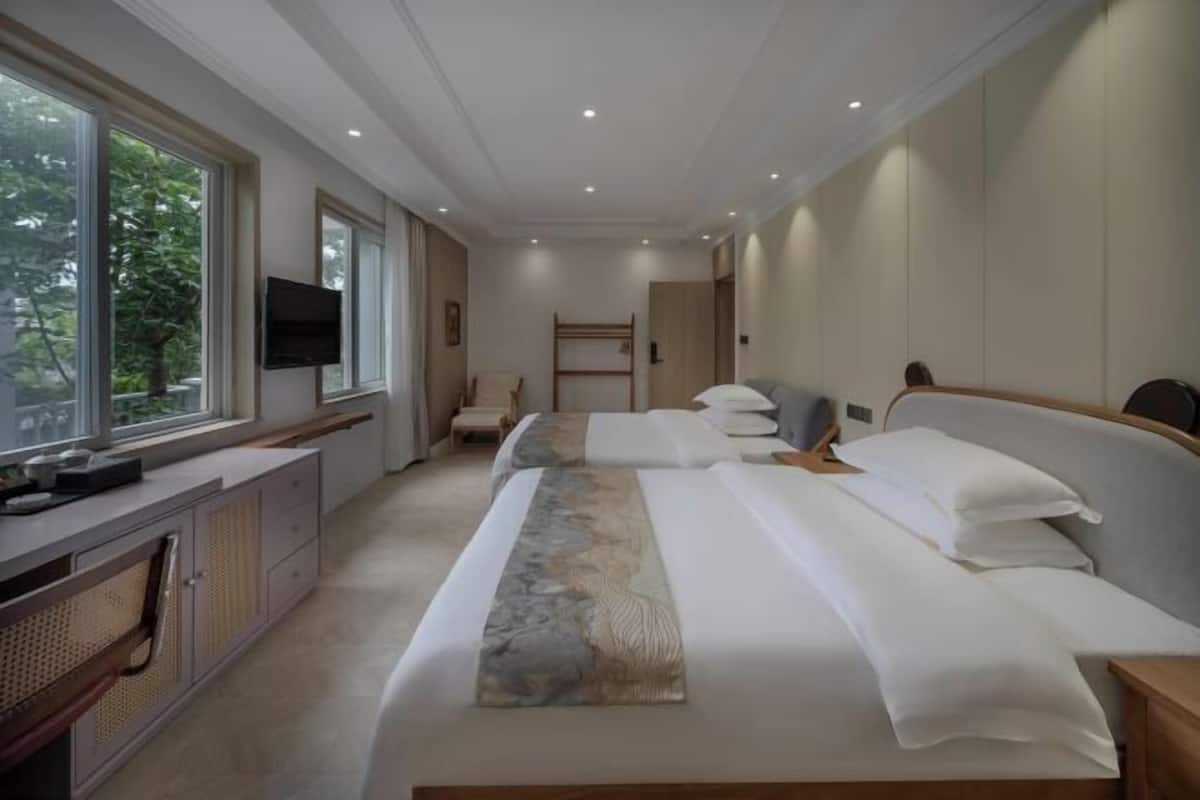 A modern hotel room with a large bed, a TV, a desk, and a window with a view of trees.