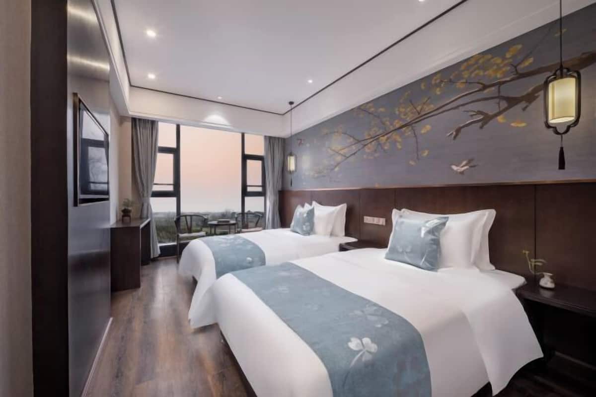 A hotel room with two beds, a desk, and a view of the outdoors.