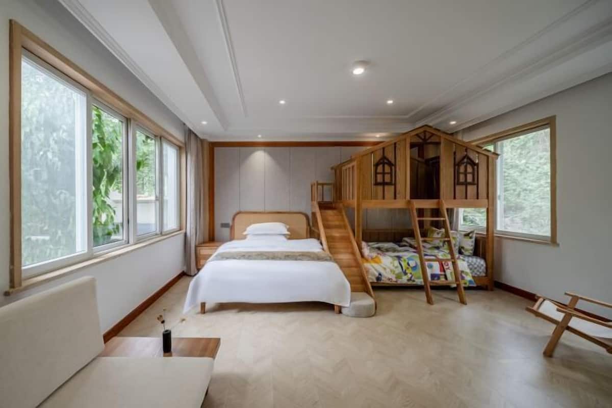 A bedroom with a bed, a wooden bunk bed, a sofa, and large windows.
