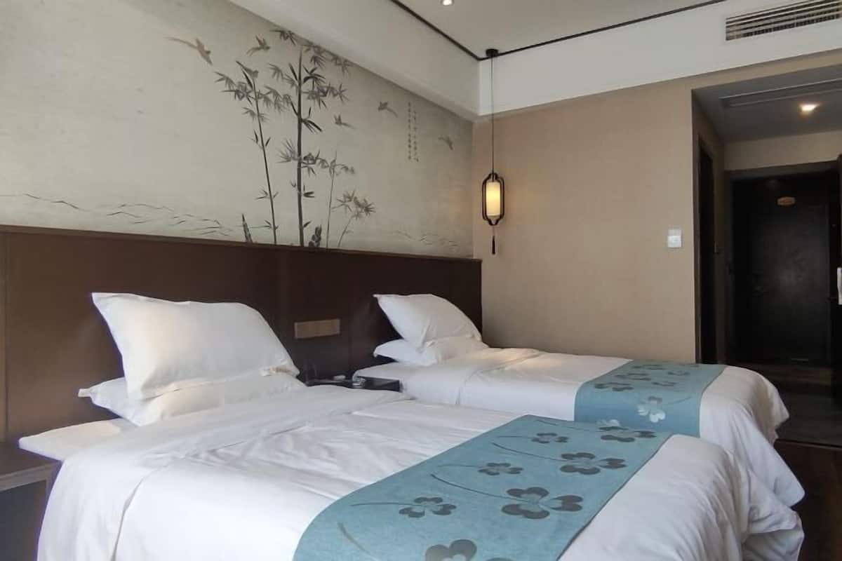 A hotel room with two beds, a wall mural, a nightstand, and a hanging light fixture.