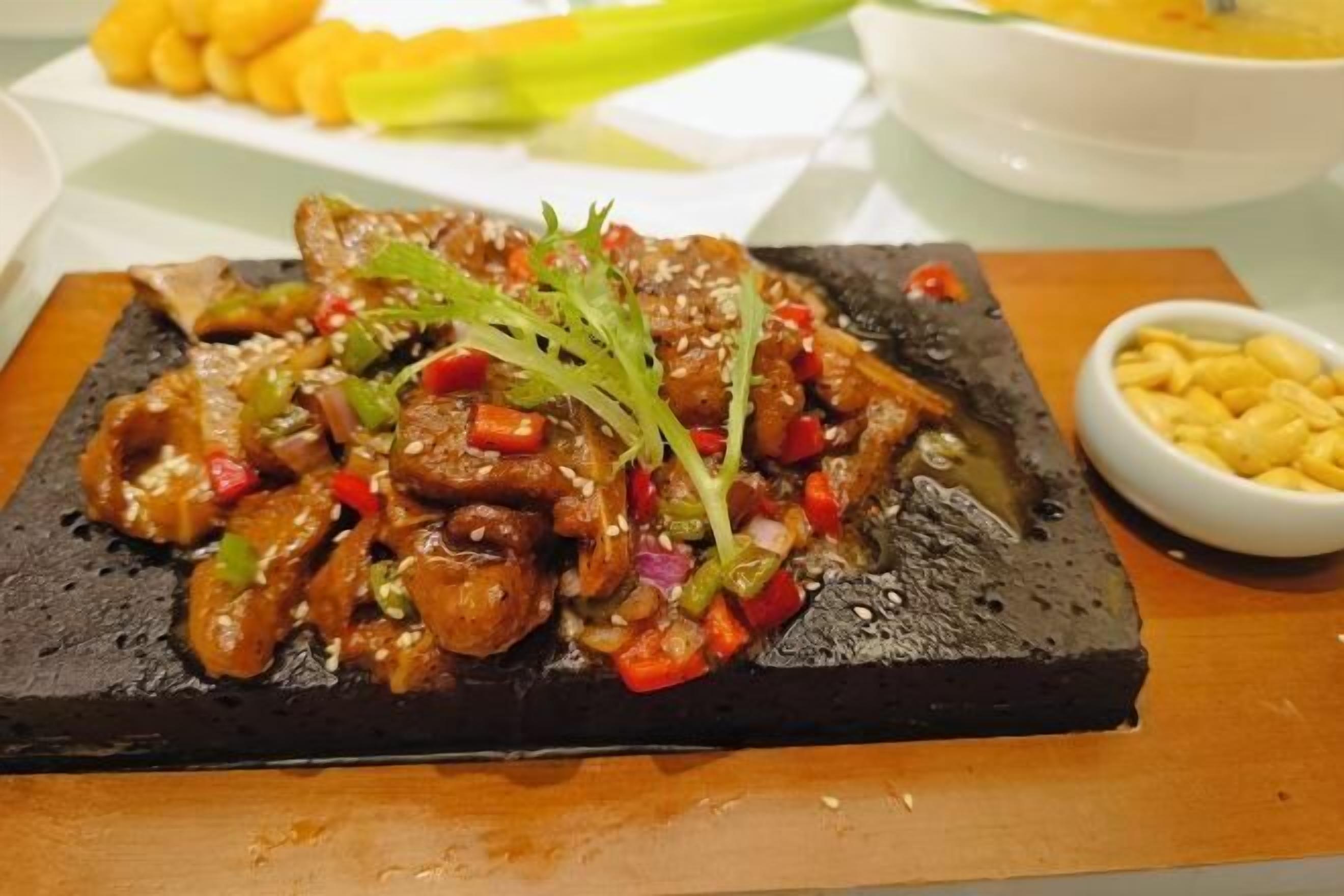 Un plat de viande sautée aux légumes, servi sur une assiette noire, accompagné d’un bol de frites.