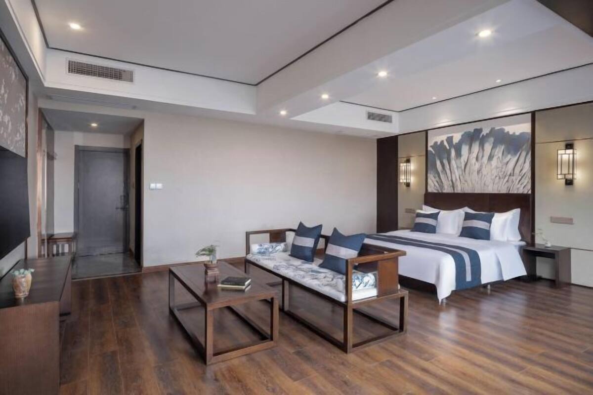 A modern hotel room with a large bed, a sofa, a coffee table, and a TV.