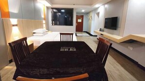 A hotel room with a bed, a TV, a dining table, and a small kitchenette.