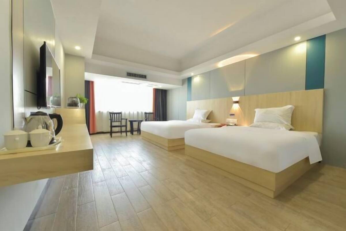 A hotel room with two beds, a desk with a chair, a TV, and a window with curtains.