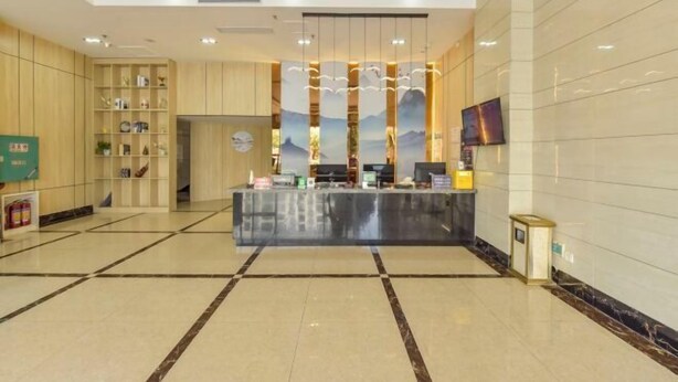 A hotel lobby with a reception desk, a TV mounted on the wall, and a decorative wall with vertical elements.