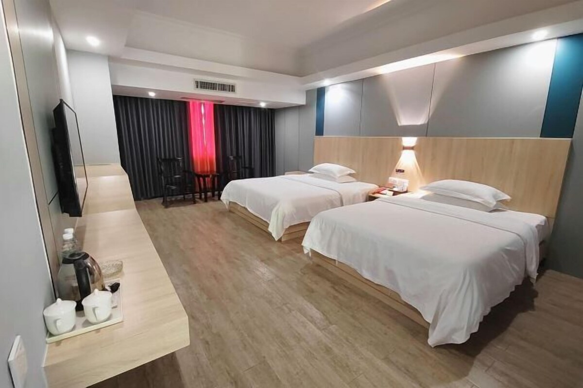 A hotel room with two beds, a desk with a lamp, a TV, and a curtain.