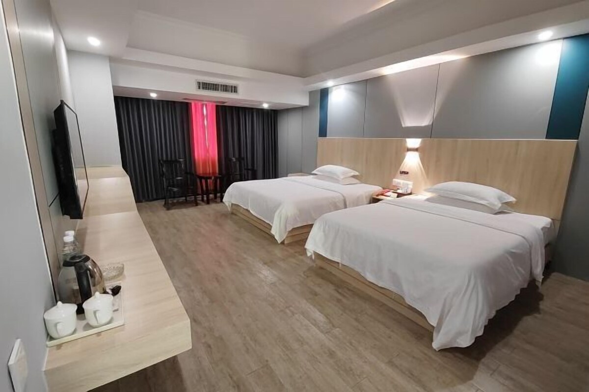 A hotel room with two beds, a desk with a lamp, a TV, and a window with curtains.