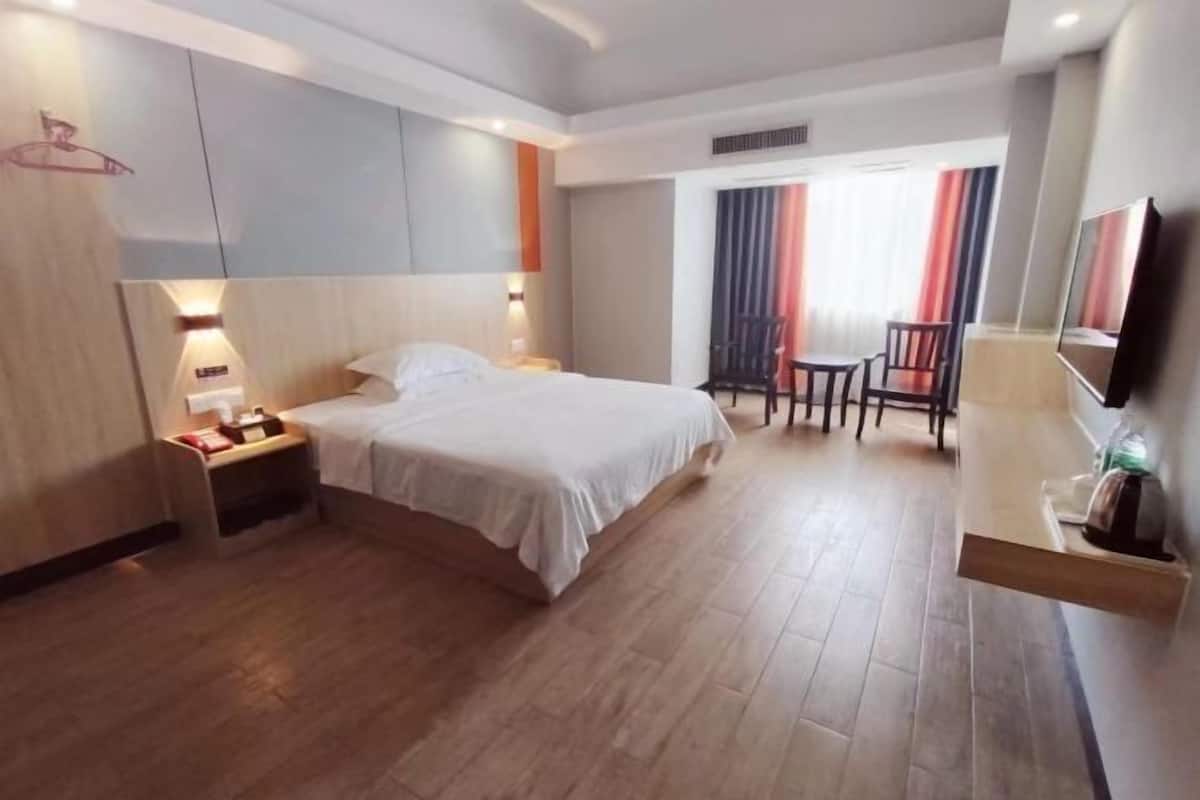 A hotel room with a bed, bedside table, lamp, chair, and a TV.
