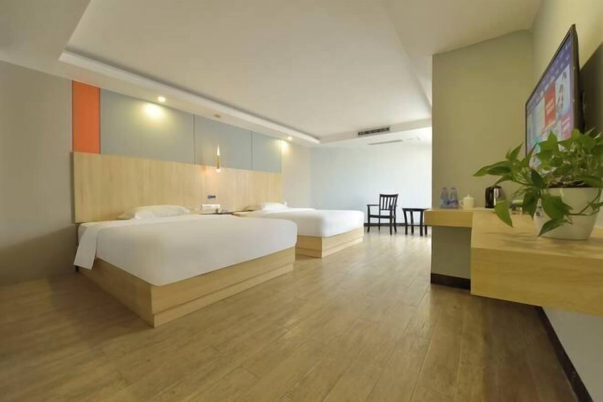 A hotel room with a wooden bed, a desk, a chair, and a potted plant.
