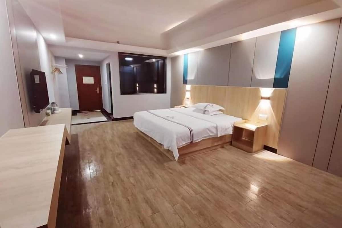 A hotel room with a bed, bedside table, lamp, wardrobe, and a desk.