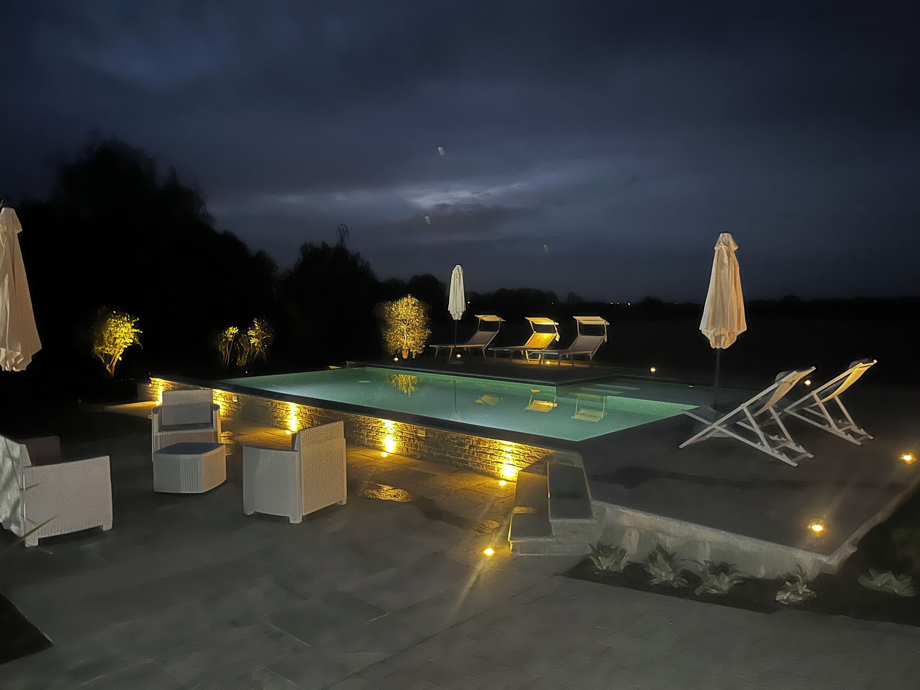 Ein Poolbereich im Freien mit Liegestühlen und Sonnenschirmen, umgeben von einer Steinterrasse.