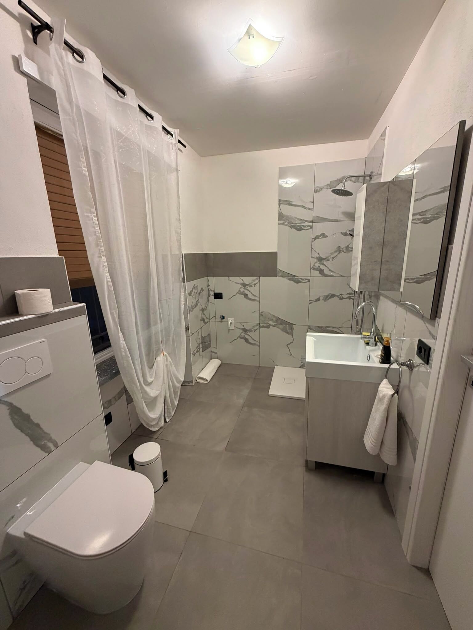 A modern bathroom with a toilet, shower, sink, and mirror.