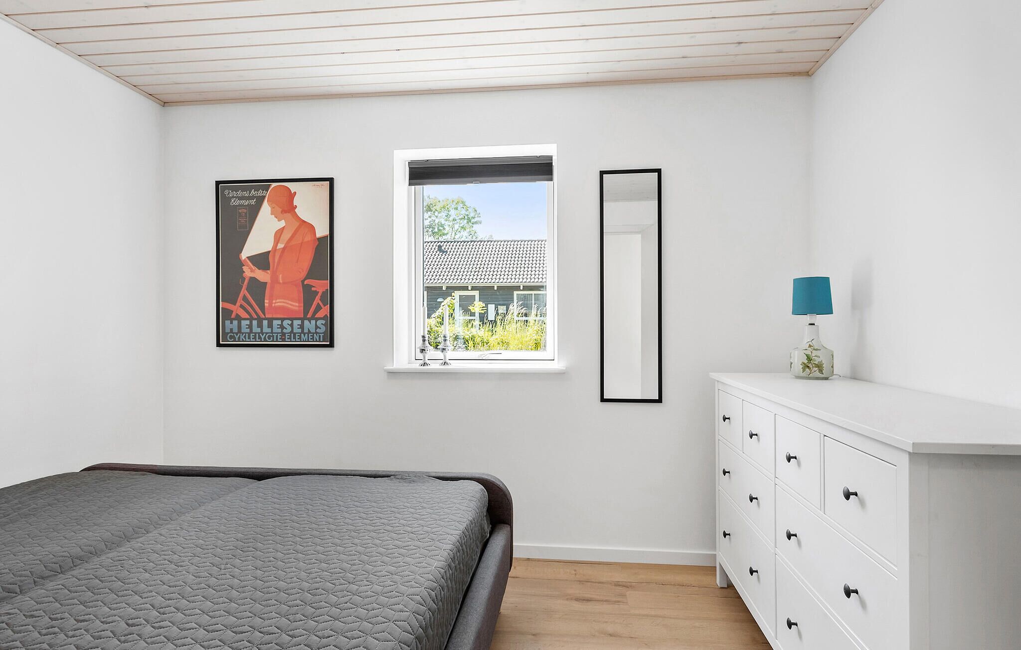 Un dormitorio con cama, cómoda, ventana con vista a una casa y un cartel en la pared.