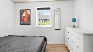 Ein Schlafzimmer mit einem Bett, einem Schminktisch, einem Fenster mit Blick auf ein Haus und einem Poster an der Wand.
