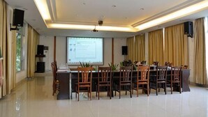 Uma sala de conferência com uma mesa grande, cadeiras, tela de projeção e alto-falantes.