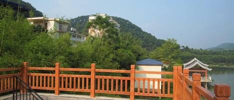 A wooden deck with a railing overlooking a body of water, surrounded by greenery and hills.