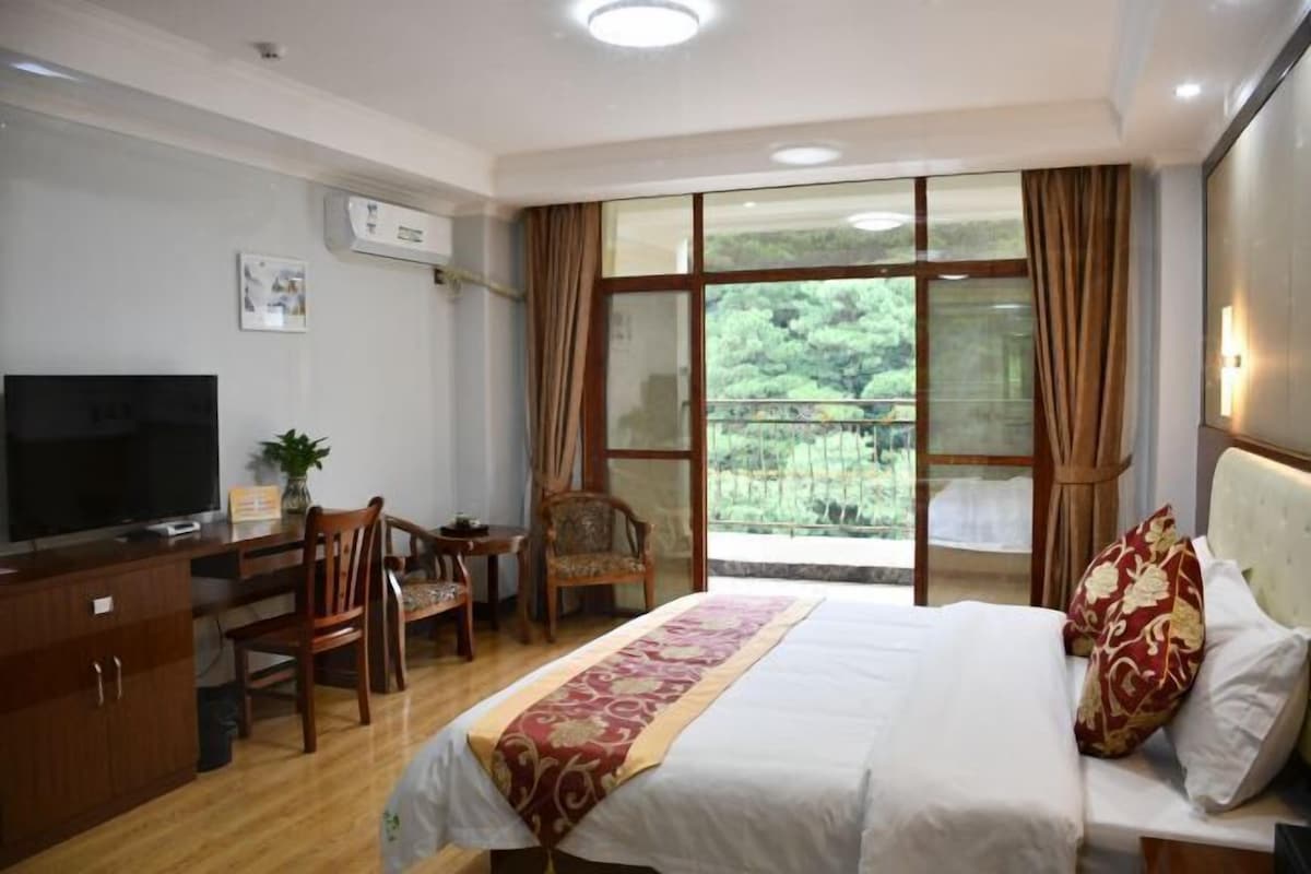Een hotelkamer met een bed, een bureau, een stoel, een televisietoestel en een balkon met uitzicht op groen.
