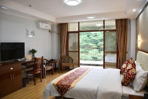 Habitación de hotel con cama, escritorio, silla, televisión y balcón con vistas a zonas verdes.