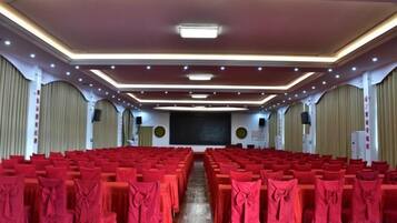 Une salle de conférence avec des rangées de tables recouvertes de nappes rouges, une scène à l’avant et un écran de projection.