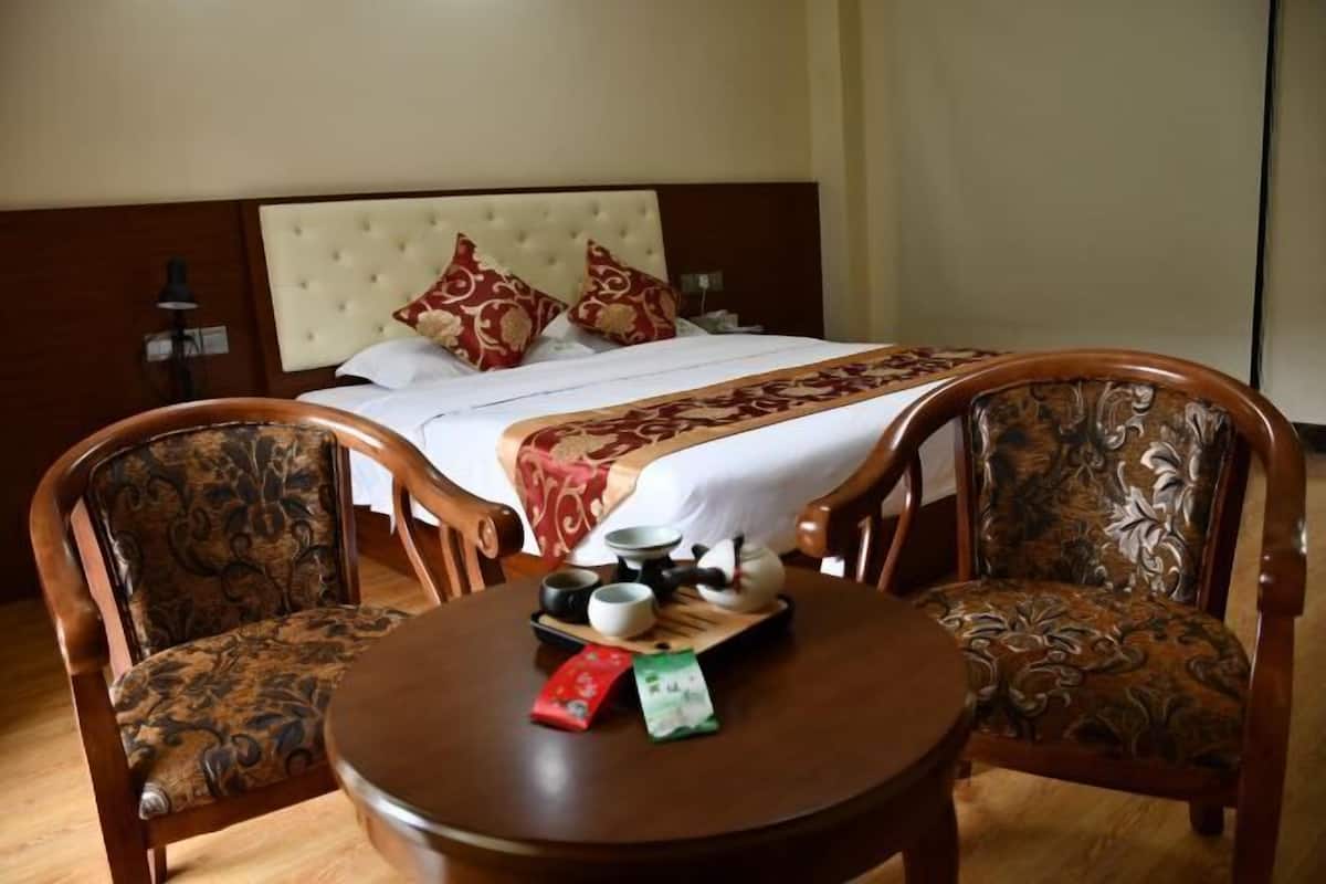 A hotel room with a bed, two upholstered chairs, a small round table with teaware, and a decorative throw blanket.