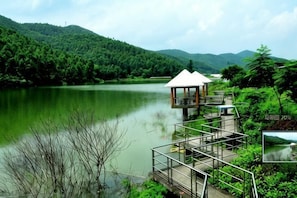 Estructura de madera junto al lago, con techo y rodeada de exuberante vegetación y colinas.