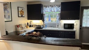 Une cuisine avec des meubles de couleur sombre, un plan de travail en bois, un évier et un four à micro-ondes.