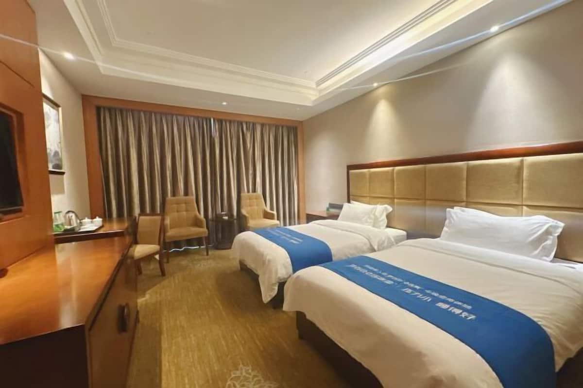 Une chambre d’hôtel avec deux lits, un bureau, une chaise et une grande fenêtre avec des rideaux.
