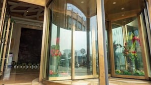 Een moderne hotelentree met een gebogen glazen gevel, een marmeren vloer en een grote sierplant.