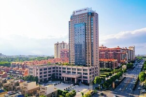 Un edificio de gran altura con varios pisos, rodeado de un estacionamiento y edificios más bajos.