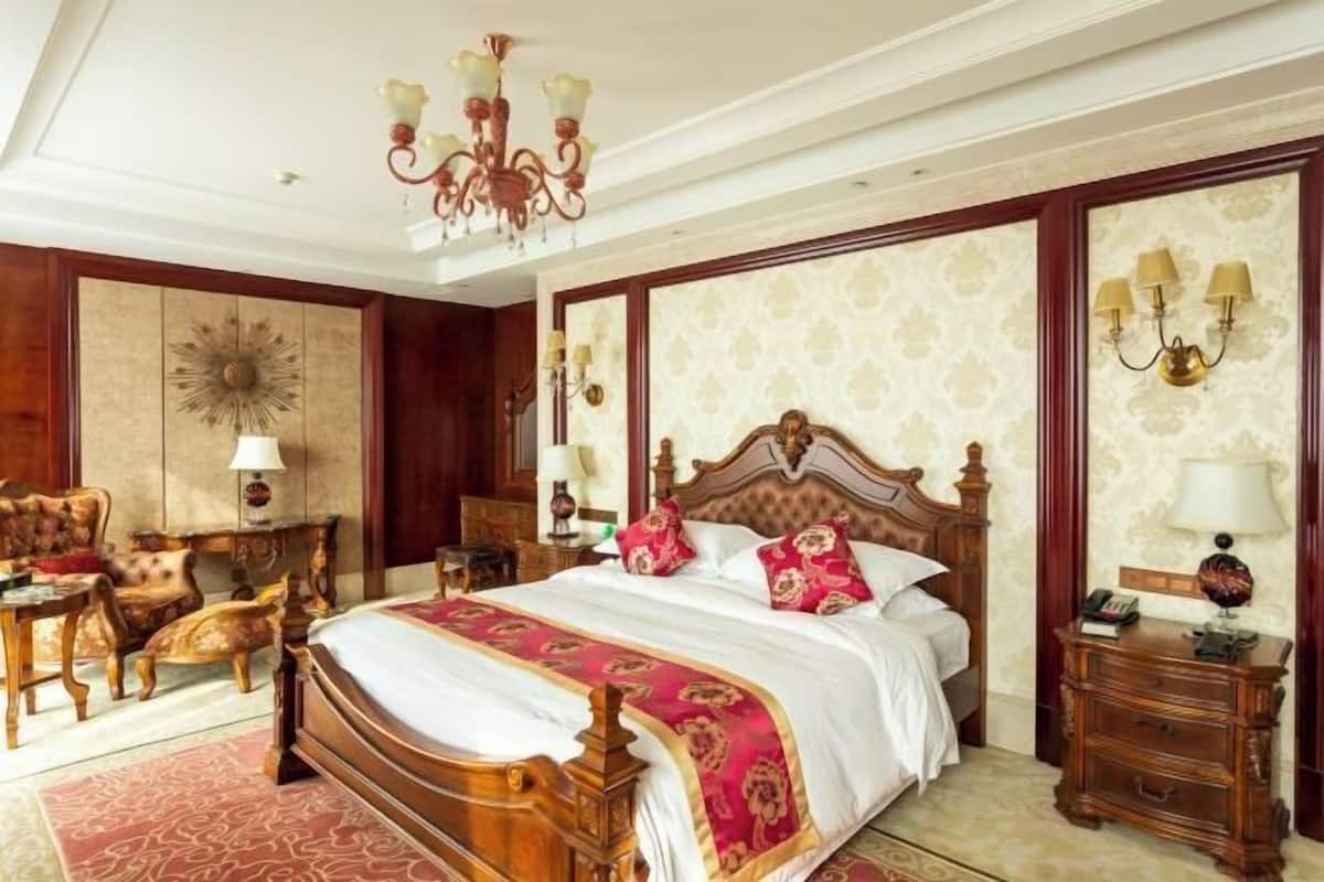 Une chambre d’hôtel classique, dotée d’un grand lit, de meubles en bois, d’un lustre et d’un papier peint à motifs.