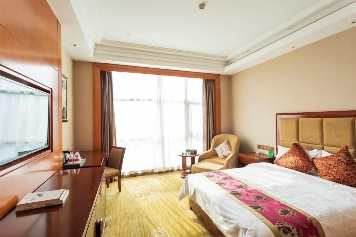 Una habitación de hotel con una cama grande, un escritorio, una silla y una ventana con cortinas.