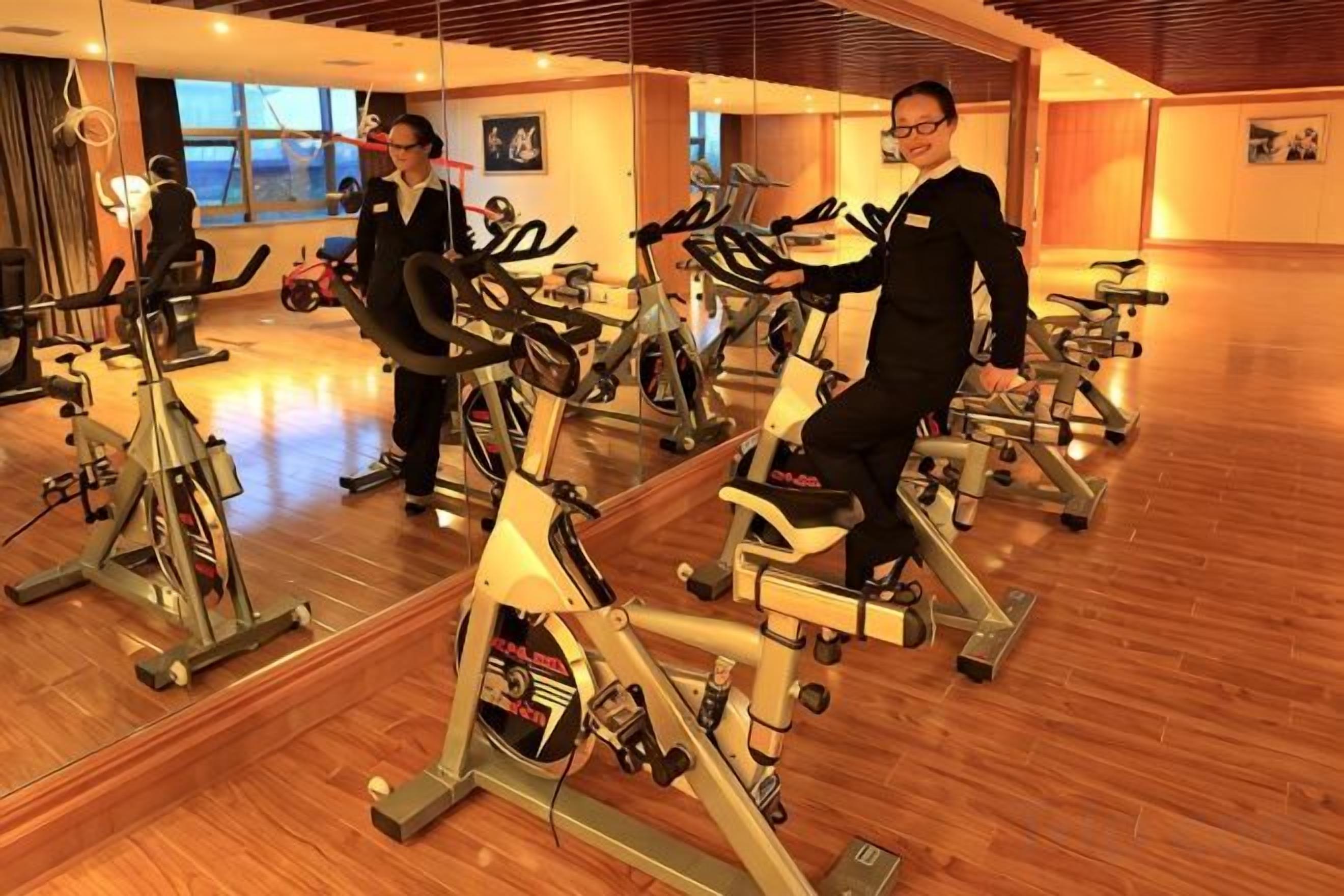 A gym with stationary bikes, mirrors, and wooden flooring.
