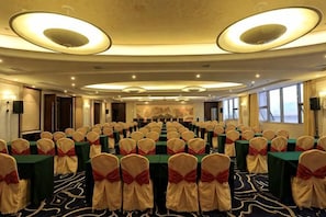 Une salle de conférence avec des rangées de tables et de chaises, de grandes fenêtres et un sol recouvert de moquette.