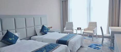 A hotel room with two beds, a large window, and a seating area with chairs.