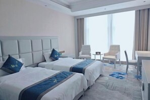 Habitación de hotel con dos camas, un ventanal grande y un área de descanso con sillas.