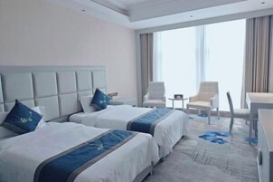 Habitación de hotel con dos camas, un ventanal grande y un área de descanso con sillas.