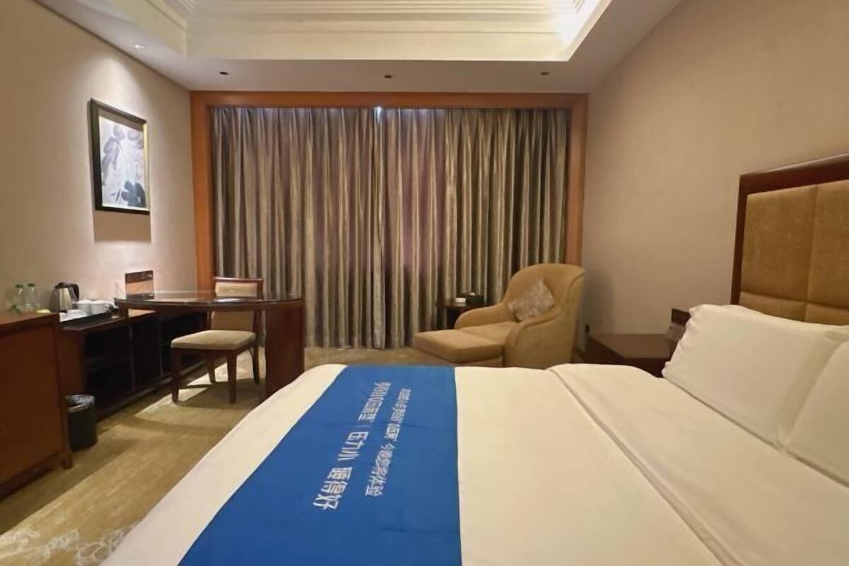 Une chambre d’hôtel avec un lit, un bureau, une chaise et une grande fenêtre avec des rideaux.