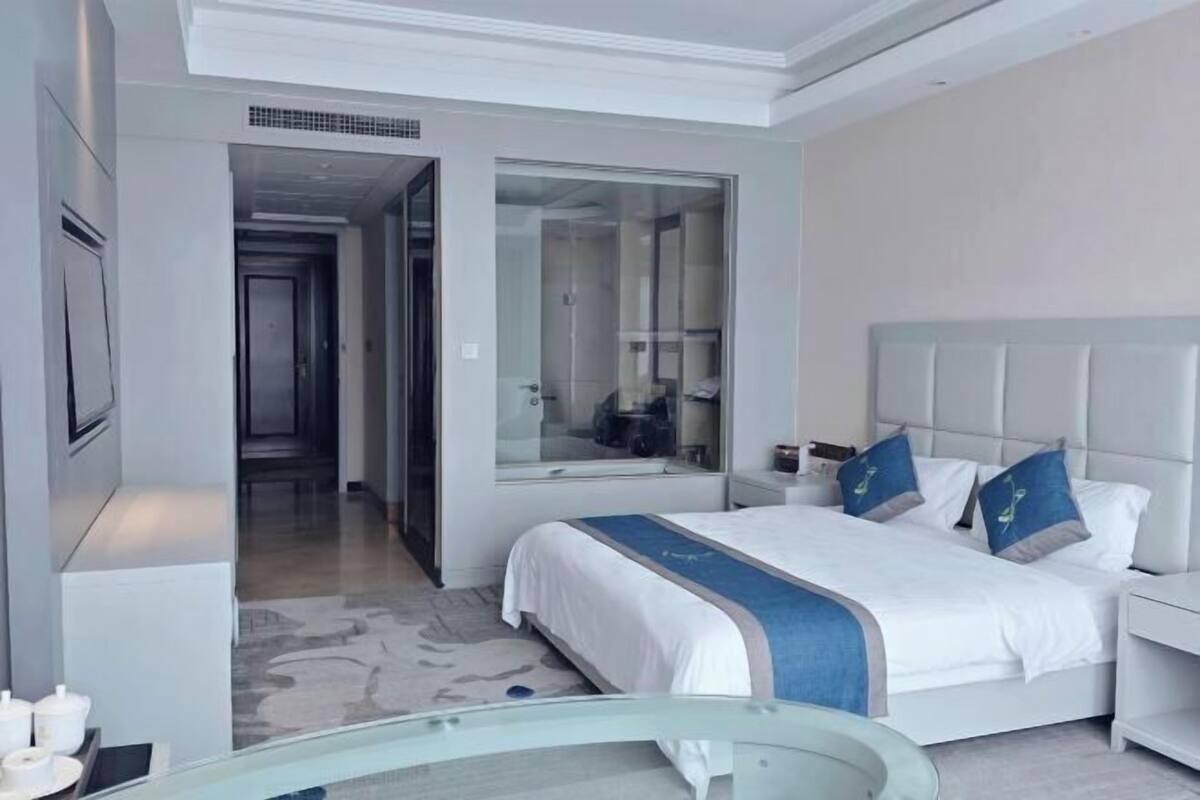 Une chambre d’hôtel moderne équipée d’un lit, d’une douche à parois de verre, d’une table de chevet et d’un grand miroir.