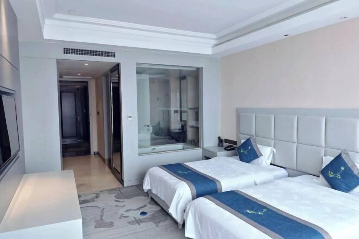 Une chambre d’hôtel avec deux lits, une cloison en verre, un téléviseur à écran plat et une petite table de chevet.
