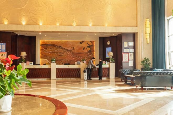 A hotel lobby with a reception desk, a large abstract mural, a blue sofa, and a potted plant.