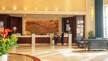 A hotel lobby with a reception desk, a large abstract mural, a blue sofa, and a potted plant.