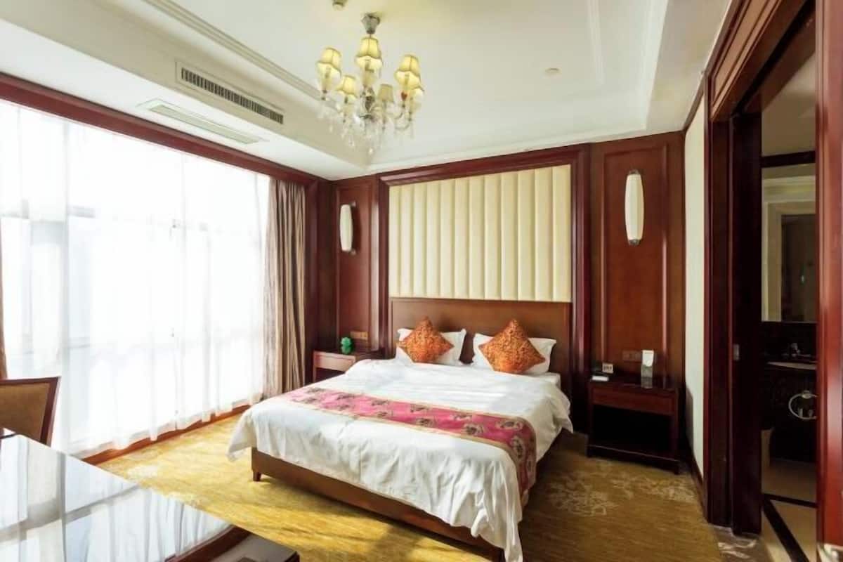 Une chambre d’hôtel avec un grand lit, un lustre, un bureau et une vue sur l’extérieur.