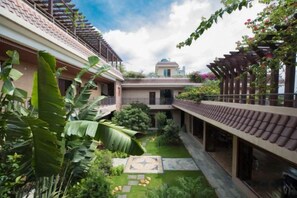 Un patio con un jardín central, un corredor cubierto y un edificio con estructura en forma de cúpula al fondo.
