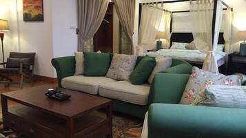 A room with a sofa, a coffee table, a bed with a canopy, and a painting on the wall.