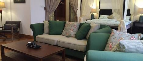 A room with a sofa, a coffee table, a bed with a canopy, and a painting on the wall.