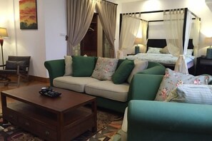 Una habitación con sofá, una mesita de centro, cama con dosel y un cuadro en la pared.