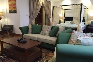 A room with a sofa, a coffee table, a bed with a canopy, and a painting on the wall.